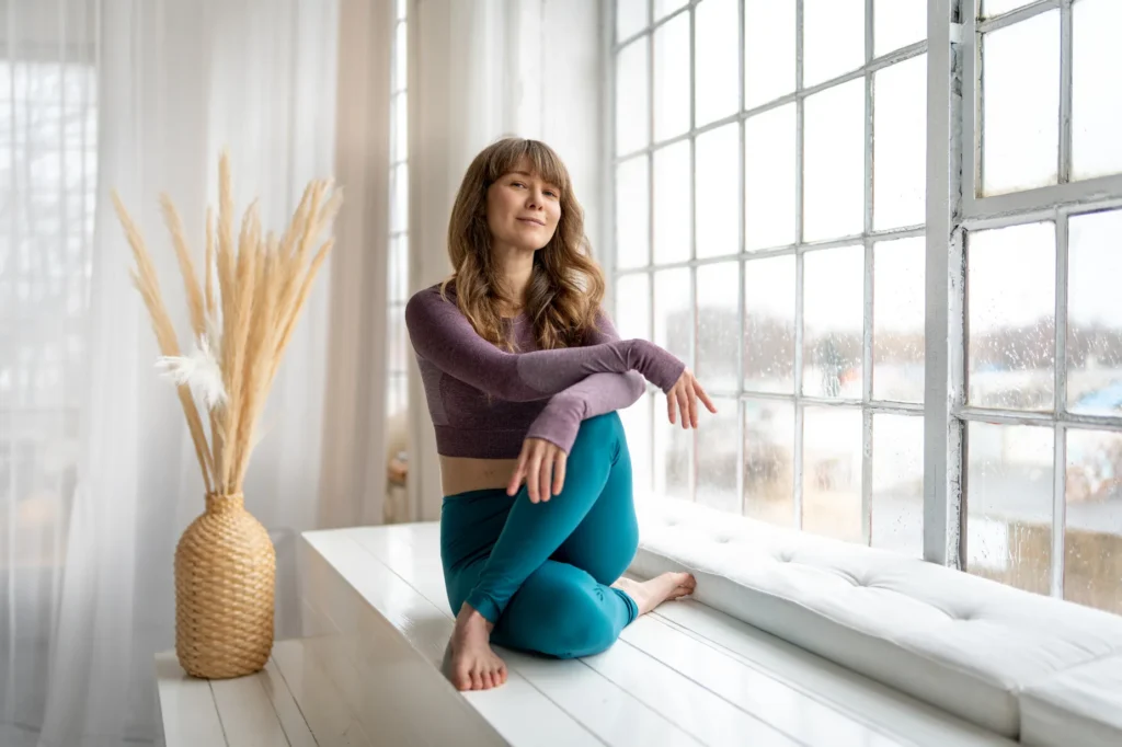 Šárka Kohoutová – kontakt pro online kurzy dynamické jógy Žena ve zkříženém sedu relaxuje před oknem