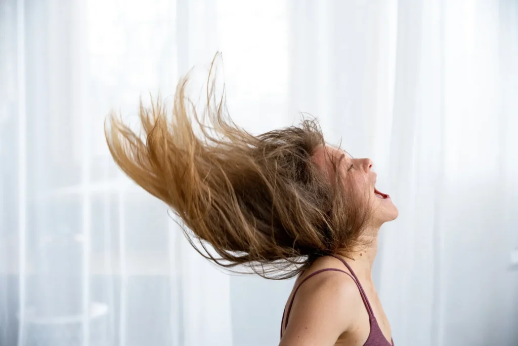 Žena v energickém pohybu s letícími vlasy a otevřenou pusou.