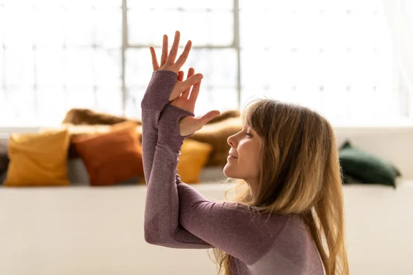 Klidná jógová pozice se spletenýma rukama. Pohled na ženu s úsměvem a propletenými pažemi.